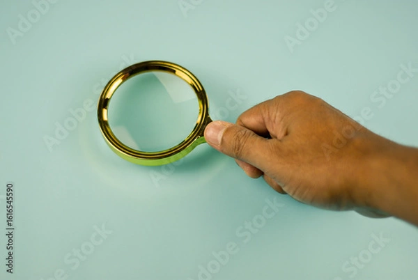 Fototapeta Hand holding a magnifying glass, focusing on the task at hand.
