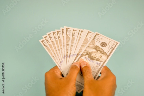 Fototapeta A hand extends, offering a stack of one hundred dollar bills.