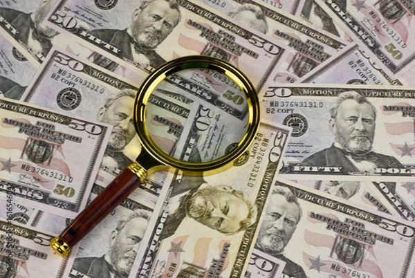 Fototapeta Fifty-dollar bills, meticulously arranged, are scrutinized by a magnifying glass.
