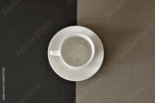 Fototapeta Empty white coffee cup and saucer on a two-toned table.
