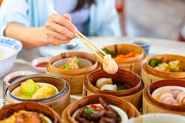 Fototapeta Young woman traveler eating traditional Chinese Dim Sum at restaurant