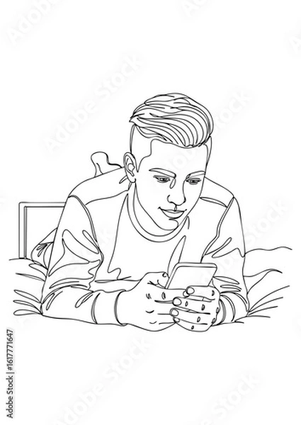 Fototapeta A young man lies on his stomach on a bed, looking at his smartphone.