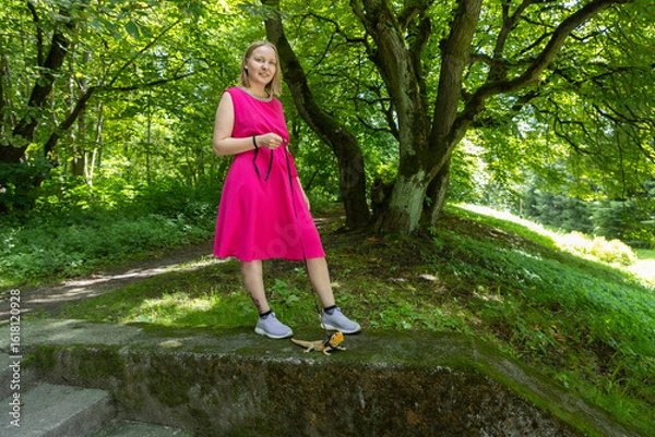 Fototapeta Young woman strolls through a summer park with her agama lizard on a delicate leash
