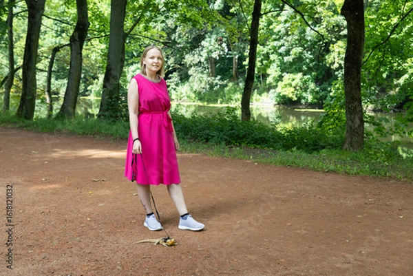 Fototapeta Young woman strolls through a summer park with her agama lizard on a delicate leash