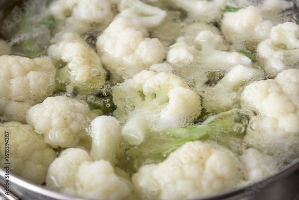 Fototapeta Fresh cauliflower is boiled in a saucepan with water. The vegetable is divided into florets and boiled in a saucepan.