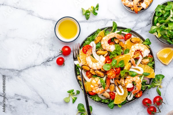 Fototapeta Delicious seafood salad with shrimp, mussels, squid, oranges, lettuce and lemon dressing, marble table, top view