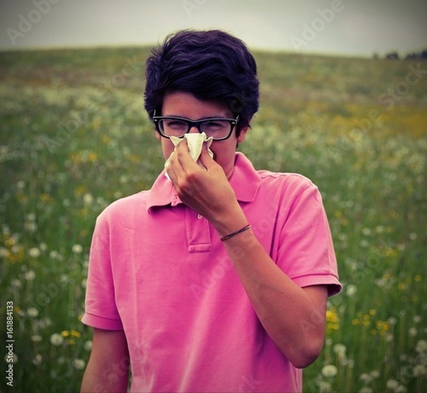 Fototapeta Allergic boy with glasses blows his nose using a white handkerch