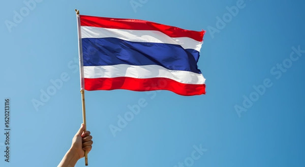 Fototapeta Patriotic Hand Holding Thailand Flag Against Bright Blue Sky