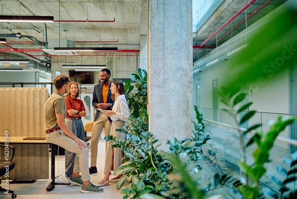 Fototapeta Group of diverse businesspeople engaged in a project discussion within a modern office filled with lush plants, fostering collaboration and creativity