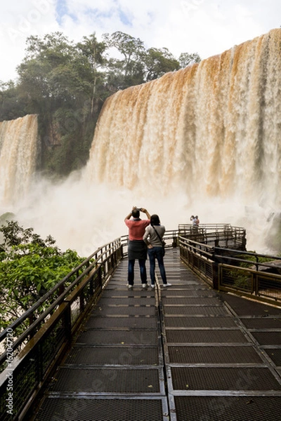 Fototapeta tourists in the footbridge at iguazu falls veiw from argentina