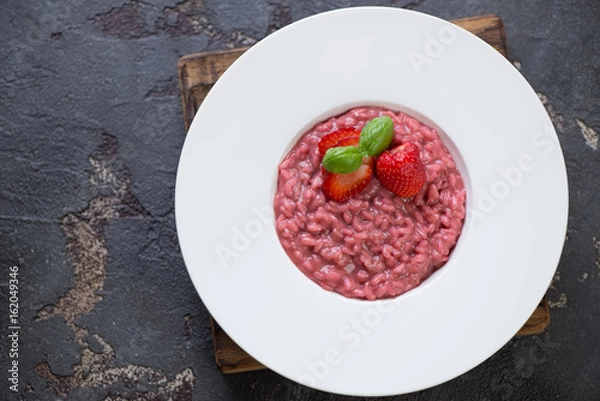 Fototapeta Powyżej widok białego talerza z risotto truskawkowym na brązowym tle kamienia, poziome ujęcie