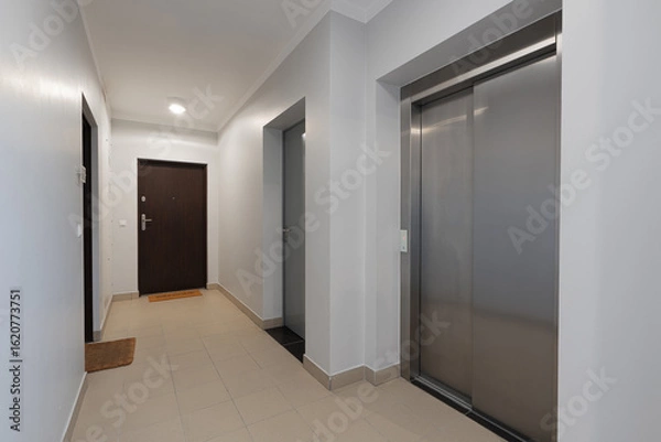 Fototapeta Interior of a modern apartment building hallway with a stainless steel elevator and entrance doors. This empty common corridor in a new residential complex is a perfect real estate background.