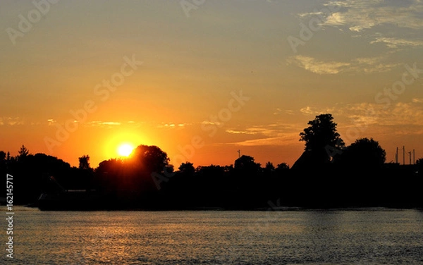 Obraz Sunset with city and threes in front of river.