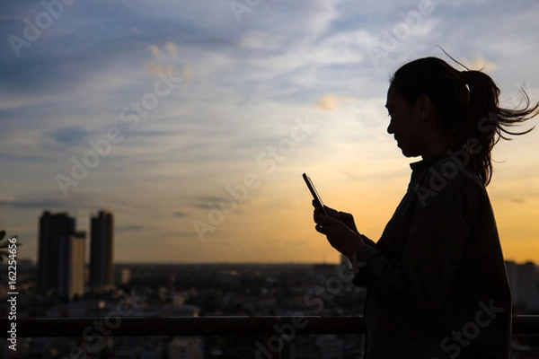 Obraz Silhouette of a woman use mobile phone in city background