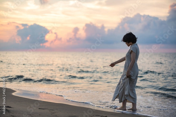 Obraz 夕暮れの海辺で花火を楽しむ女性モデルの柔らかなボケ感を活かしたポートレート