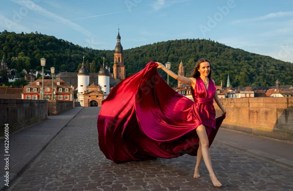 Fototapeta schöne Frau in rotem Kleid, tanzt in Heidelberg in der Morgensonne, über die alte Brücke.