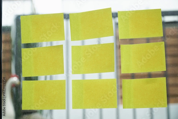 Fototapeta Yellow sticky notes are neatly arranged on glass surface, creating organized and creative display. background is blurred, emphasizing notes