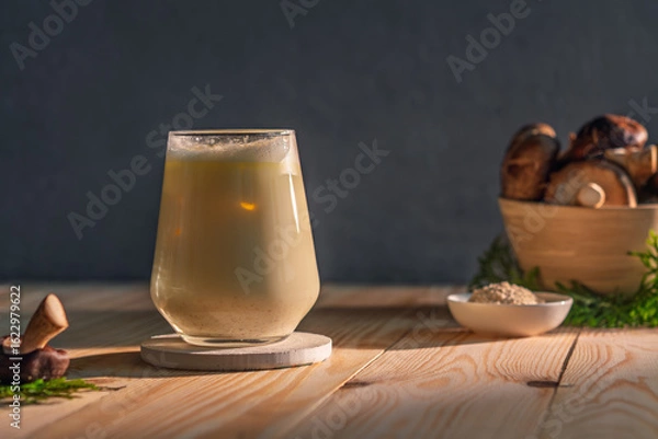 Fototapeta Iced creamy mushroom adaptogen latte in a clear glass stands on a rustic wooden table in sunlight, evoking freshness and modern wellness trends.