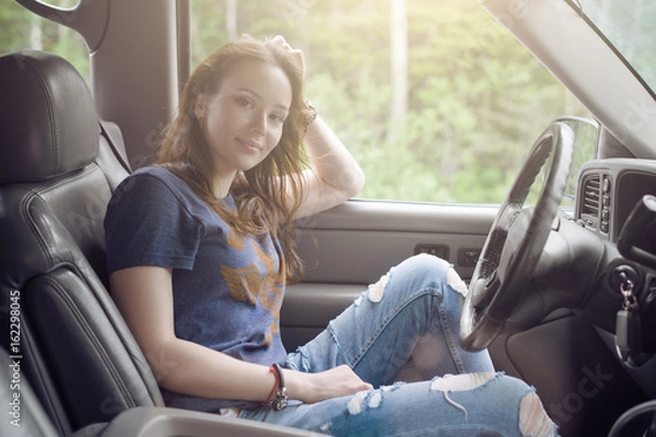 Fototapeta Pretty girl traveler sitting in the car and resting from a long journey in Sunny weather