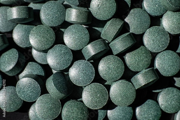 Fototapeta Close-up of black round tablets in scattered pile. Macro shot of greenish-black dietary supplement pills. Healthcare and pharmaceutical concept for design and banner