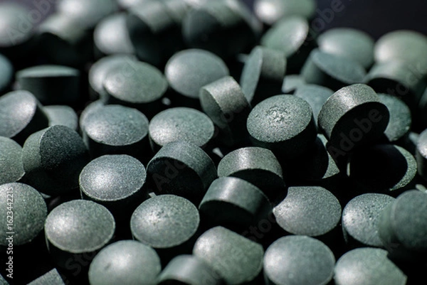 Fototapeta Close-up of black round tablets in scattered pile. Macro shot of greenish-black dietary supplement pills. Healthcare and pharmaceutical concept for design and banner