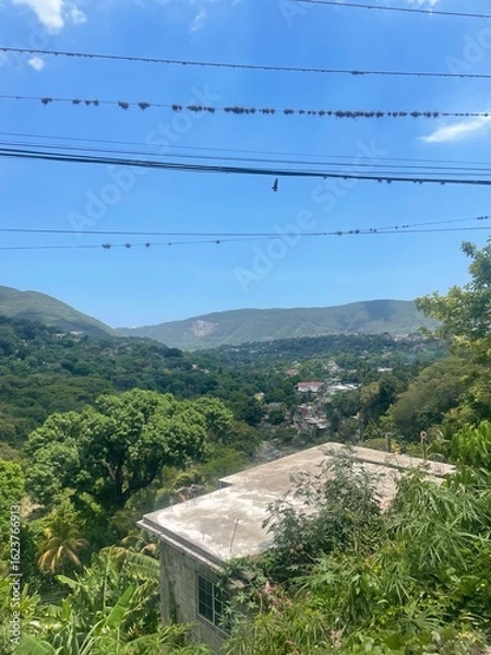 Obraz Hilltop view of a lush green valley with scattered houses and mountains in the distance under a clear blue sky.