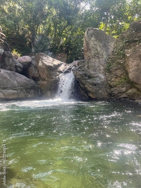 Obraz Small waterfall cascading into a clear green pool, surrounded by rocks and tropical forest — a peaceful natural retreat.