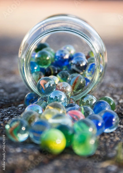 Obraz Glass jar full of crushers, fallen on the street. Front view of jar.
Bright picture, with blue as main color.
Front and background blurred.
Other colors red, green, yellow.