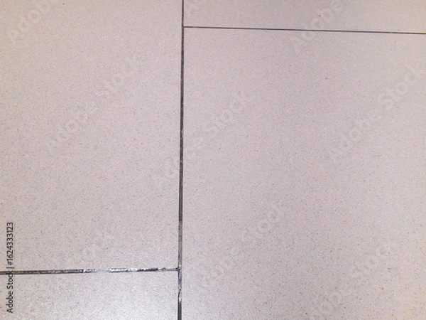 Fototapeta A close-up view of a clean, light gray floor tile with fine speckles and visible grout lines, creating a minimalist and seamless texture.