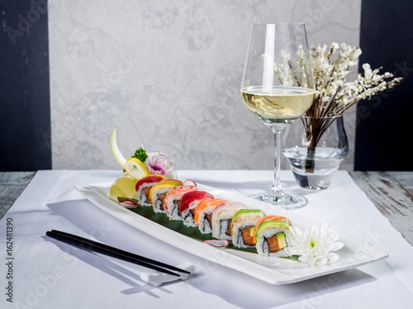 Obraz Rainbow sushi roll with salmon and avocado, complete with a glass of white wine and a tempura decoration