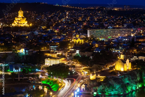 Fototapeta Night panorama view of Tbilisi, capital of Georgia country. Holy Trinity Cathedral (Sameba) and Metekhi church at night with illumination and moving cars.