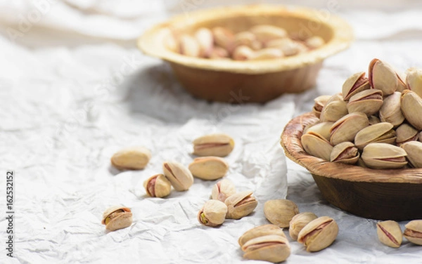 Fototapeta There are two brown bowl filled with pistachio filled in it. one bowl is in the front and in the background another bowl of pistchio is placed and it is shot on white background.