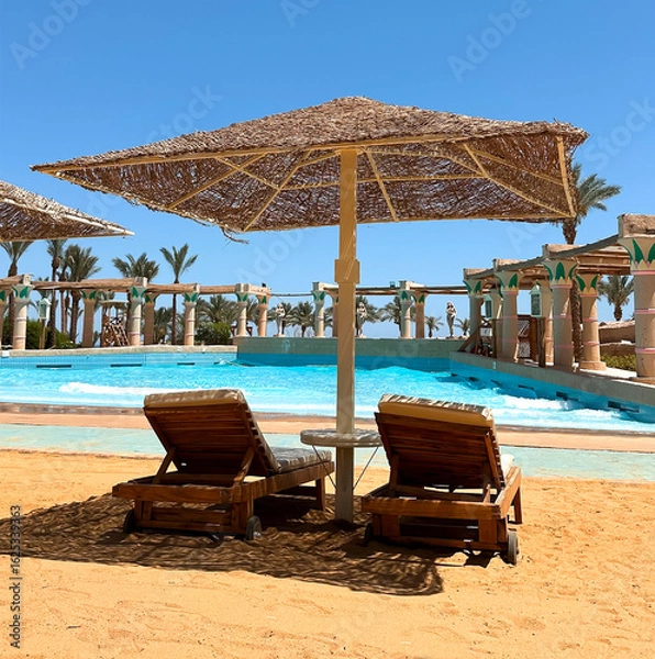 Obraz Wooden sun loungers and a straw beach umbrella by the pool. Artistic composition