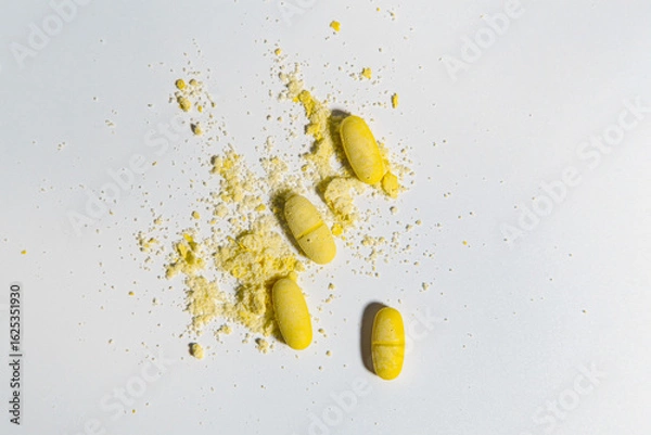 Fototapeta top view of light background and yellow tablets with scattered powder