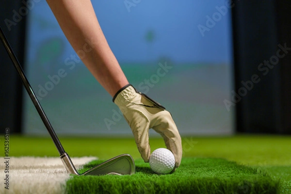 Fototapeta Golfer Hand with Glove Placing Ball on Artificial Turf in Indoor Golf Simulator Training Facility