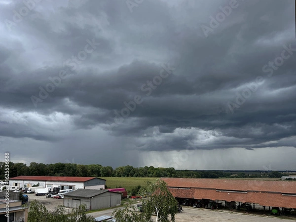 Fototapeta Storm clouds over the landscape. View of an agricultural environment with garages and fields.