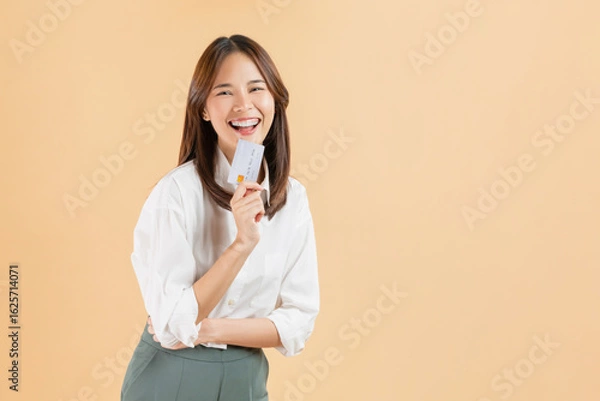 Obraz Cheerful beautiful Asian woman holding credit card isolated on beige color background.