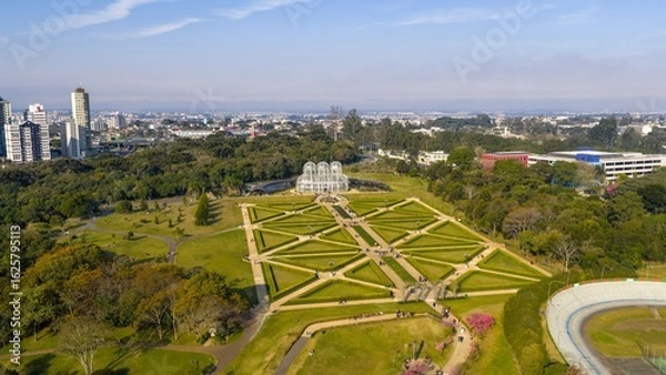 Obraz Oblique drone view of Curitiba Botanical Garden with symmetrical paths, greenhouse, and city in the background.