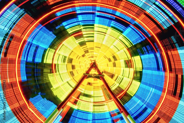 Fototapeta A dynamic low-angle long exposure of a spinning Ferris wheel at night, creating a vibrant, abstract vortex of colorful red, yellow, and blue light trails at an amusement park