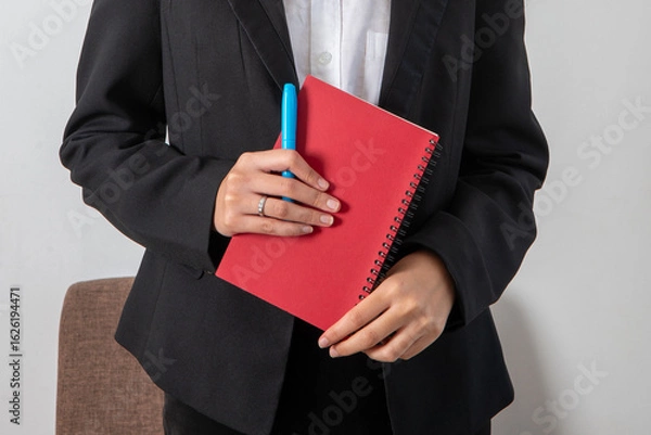 Obraz Businesswoman in black suit holding red book in hands.