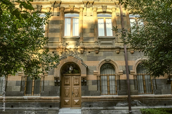 Fototapeta Old building of multicolored tufa stone with carved arches,columns and cornices surrounded by trees