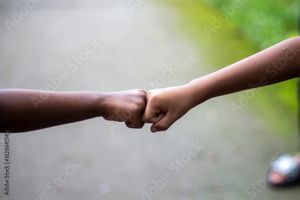 Fototapeta Two boys shaking hands with clenched fists and the background behind them is blurred