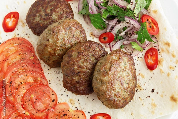 Fototapeta kuru kofte on flat bread garnished with tomatoes, chili and salad of red onion and parsley