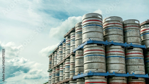 Obraz Stacked metal beer kegs under a cloudy sky