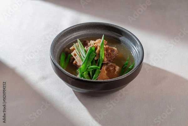 Fototapeta A rich and comforting bowl of clear oxtail beef broth soup, generously garnished with fresh green onions and tender meat, perfect for a warming meal