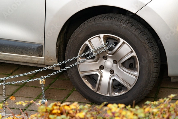 Fototapeta Car wheel wrapping in thick chain. Control, bureaucracy and administrative enforcement. Urban crime prevention and anti-theft protection in urban areas. Radical security measures against theft