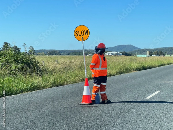 Obraz Road worker stand beside a slow down traffic sign