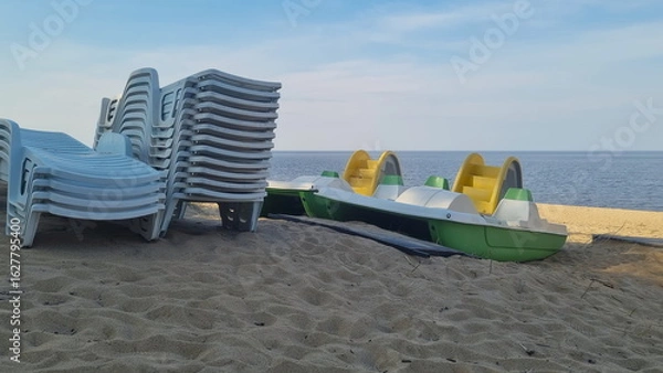 Fototapeta Stack of sun loungers on the beach.  Start or end of the summer season at the resort city. Heap of sunbeds at the coastline.