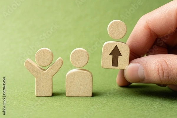 Fototapeta Hand placing a wooden figure with an upward arrow, signifying career advancement,  amongst two other figures