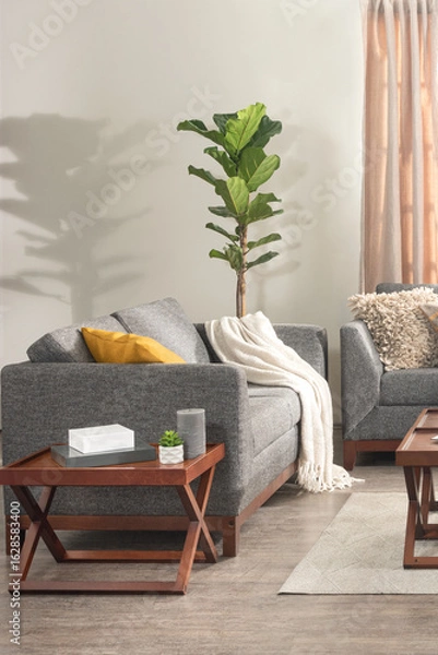 Fototapeta Mid-century inspired living room scene with grey upholstered sofas, mustard and ivory cushions, wood accent table, indoor fiddle leaf fig plant, and warm natural lighting creating a cozy mood